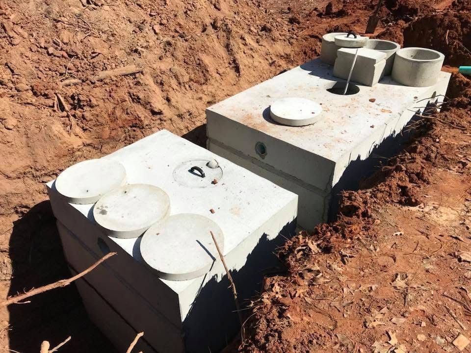 Two concrete septic tanks set in a red-clay excavation